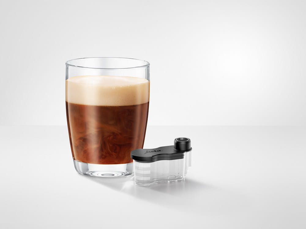 JURA Sirupaufsatz für Kombiauslauf 25069 neben einem Glas Kaffeespezialität